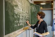 Lehrerin schreibt mit aufgeklappten Buch in der Hand etwas Französisches an die Tafel Lehrerin schreibt mit aufgeklappten Buch in der Hand etwas Französisches an die Tafel
